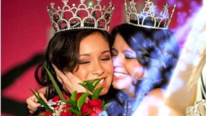 two pageant girls wearing a crown; hugging at a beauty pageant; red background for miss sparkle success pageant; annie eure